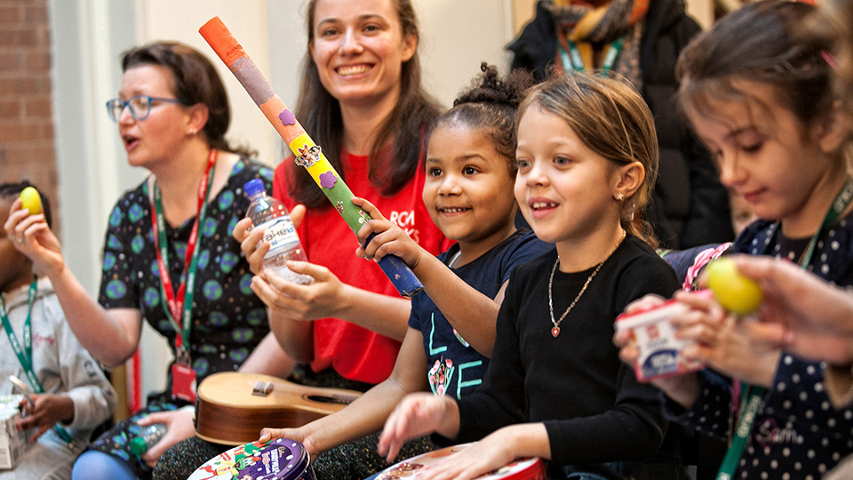 Children and adults at an RCM Sparks events, smiling and playing recycled instruments Children and adults at an RCM Sparks events, smiling and playing recycled instruments
