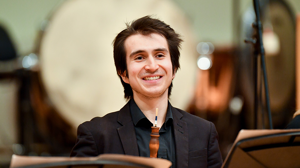 An RCM student holding a historical oboe and smiling in rehearsal