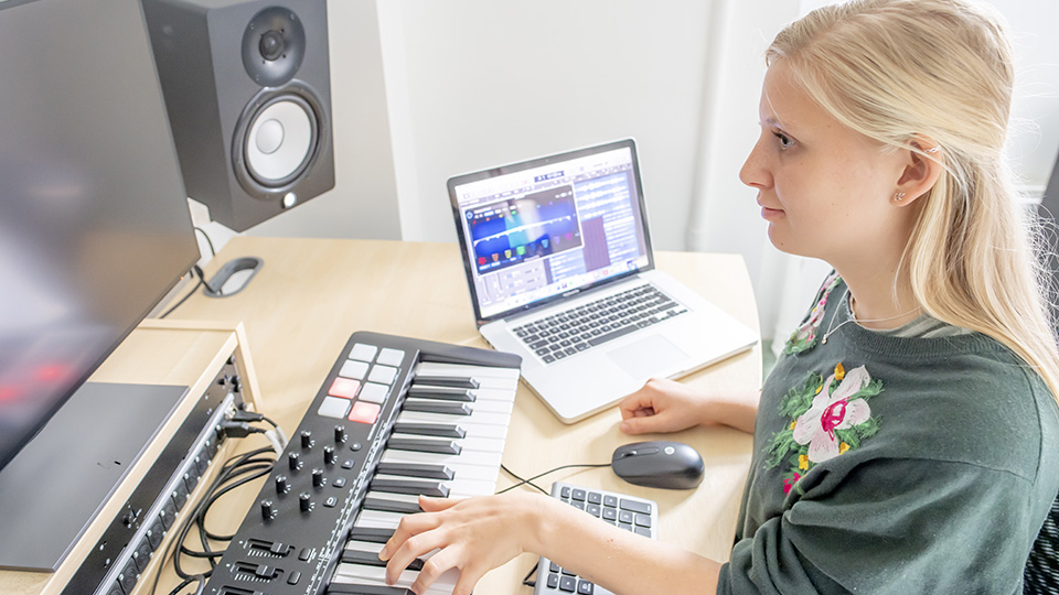 A student using a keyboard attached to a computer to compose, looking at the computer screen