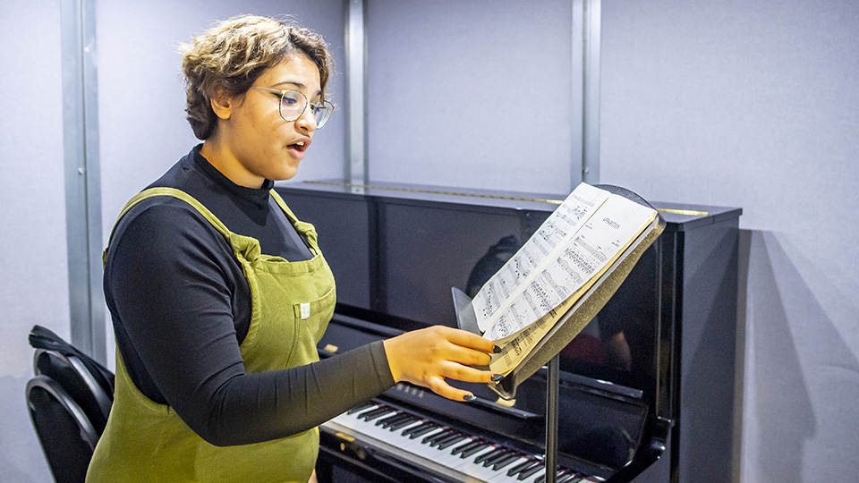 An RCM student standing and singing next to a piano An RCM student standing and singing next to a piano