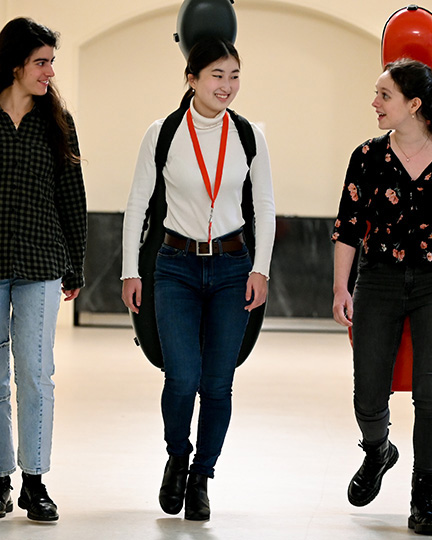 A group of students, wearing casual clothing, carrying instruments, laughing and