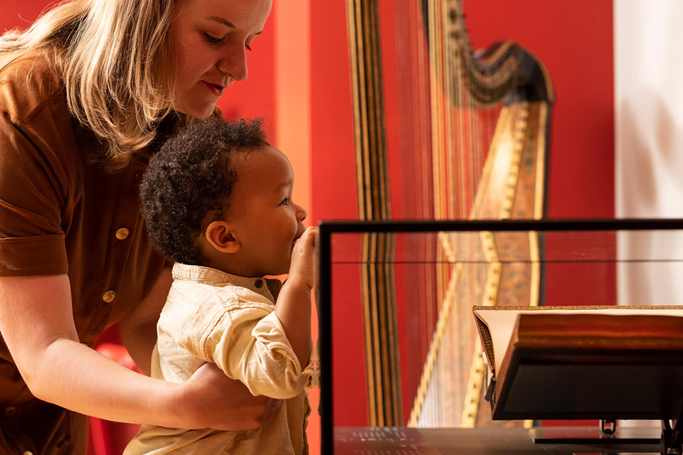 A young black boy, holding onto a glass case, looking at an exhibit, with a white women, holding him up to look at it, at the museum.