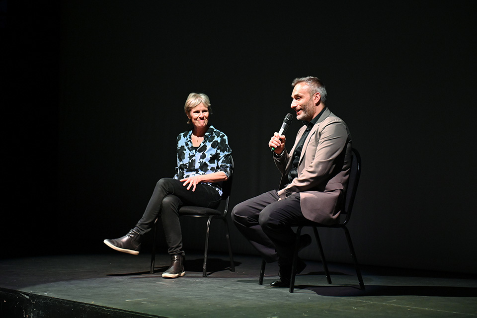 Dimitri Scarlato holding a microphone, sat on stage next to Rachel Portman, composer
