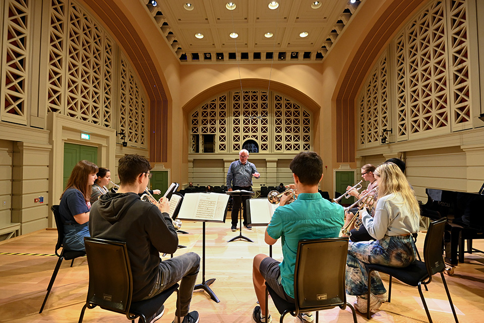 Looking out on stage at a conductor and small ensemble in rehearsal, in the RCM's Performance Hall