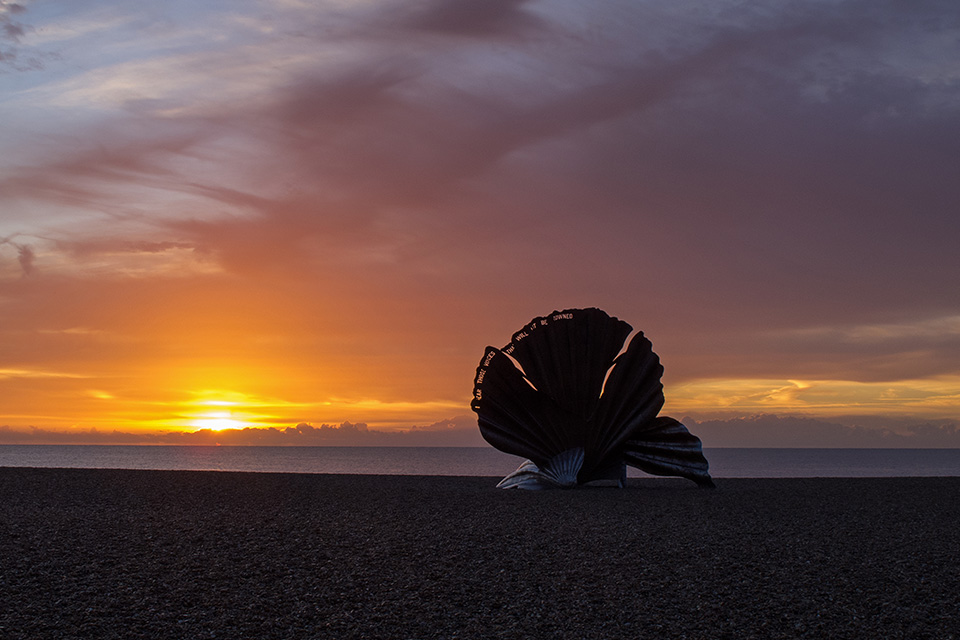 A large statue on a beach at sunset