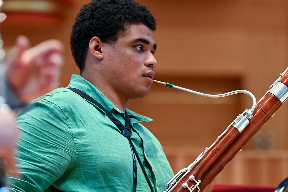 A young man plays the bassoon on stage