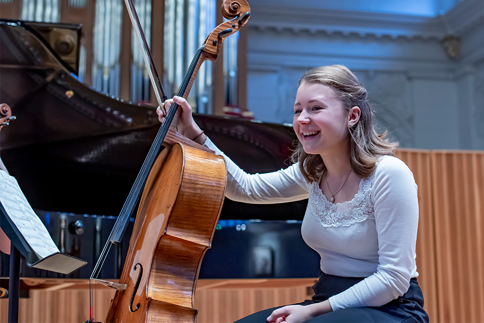 A woman holds her cello and laughs