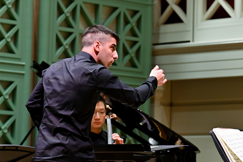 A man wearing a black shirt conducts animatedly on stage