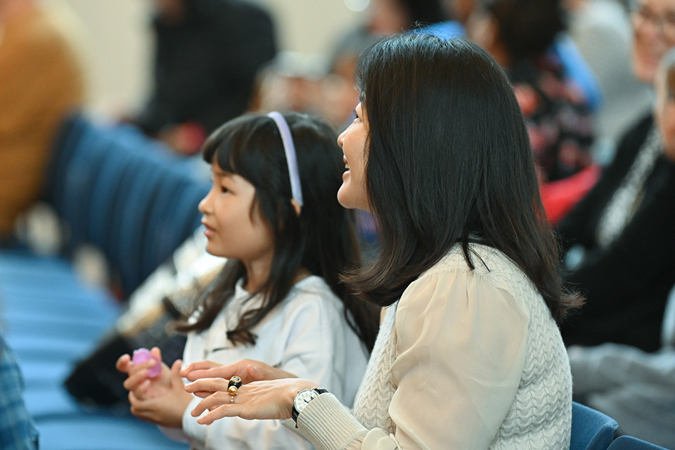 A young girl and mother sit in an audience smiling