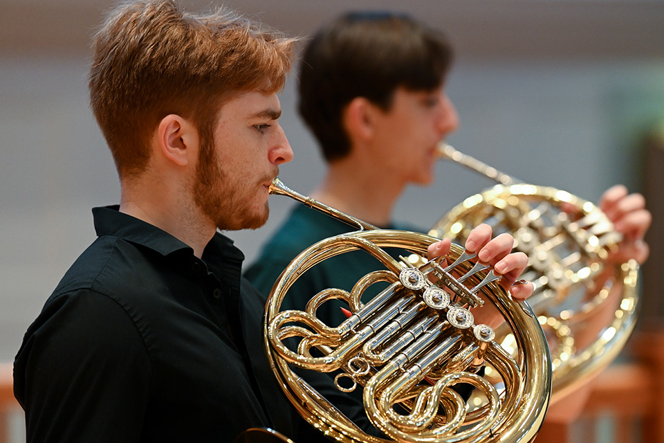 A man in a black shirt plays the horn on stage