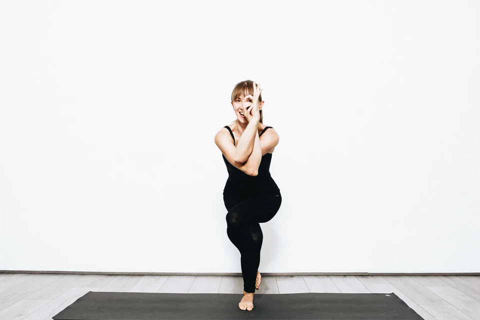 Flo Yoga poses on a yoga mat, smiling between her fingers