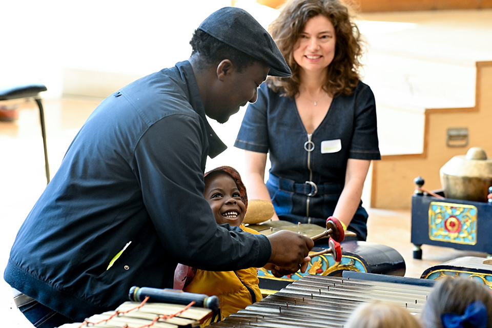 A young boy laughs as he plays the xylophone with an adult