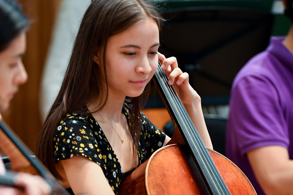 A young girl plays the cello in an orchestra