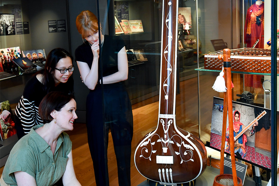 Three people look attentively at a historical musical instrument in a display case