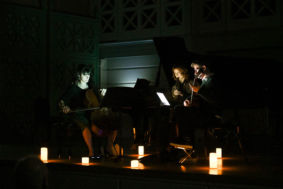 A chamber group perform on a dark stage lit up by candles on the floor