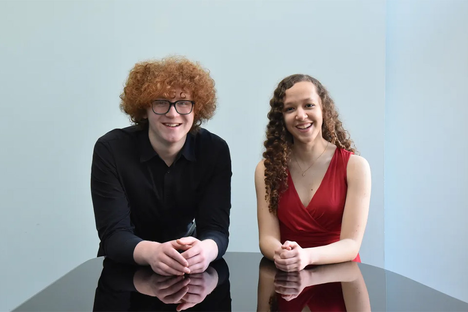 Aurelia Walker and Anthony Zemsky lean on a piano and smile