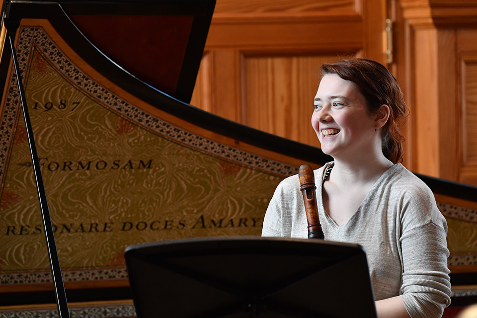 A young woman holds her recorder and smiles
