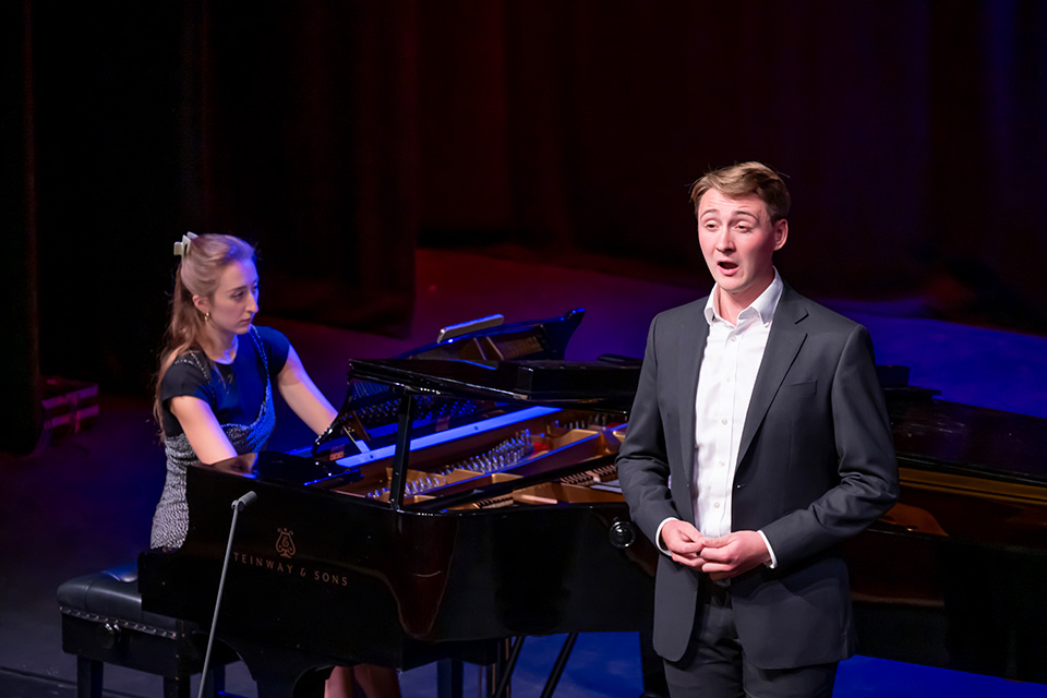 A singer performs on stage in the Britten Theatre, a pianist accompanying behind him