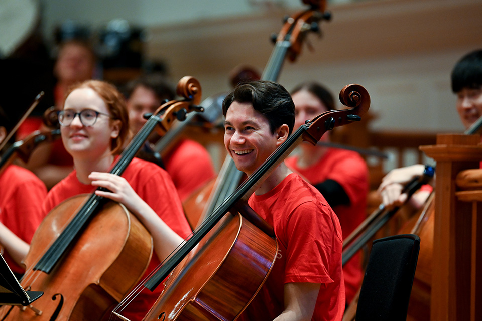 A cellist wearing a red RCM Sparks t-shirt laughs