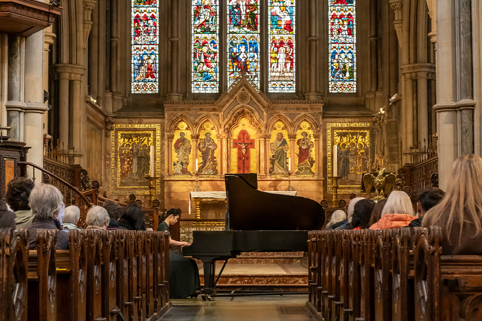 A pianist performs in the ornate St Mary Abbots Church, an audience watching from the pews