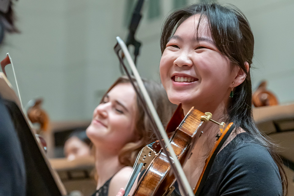 A girl laughs while holding her violin in an orchestra
