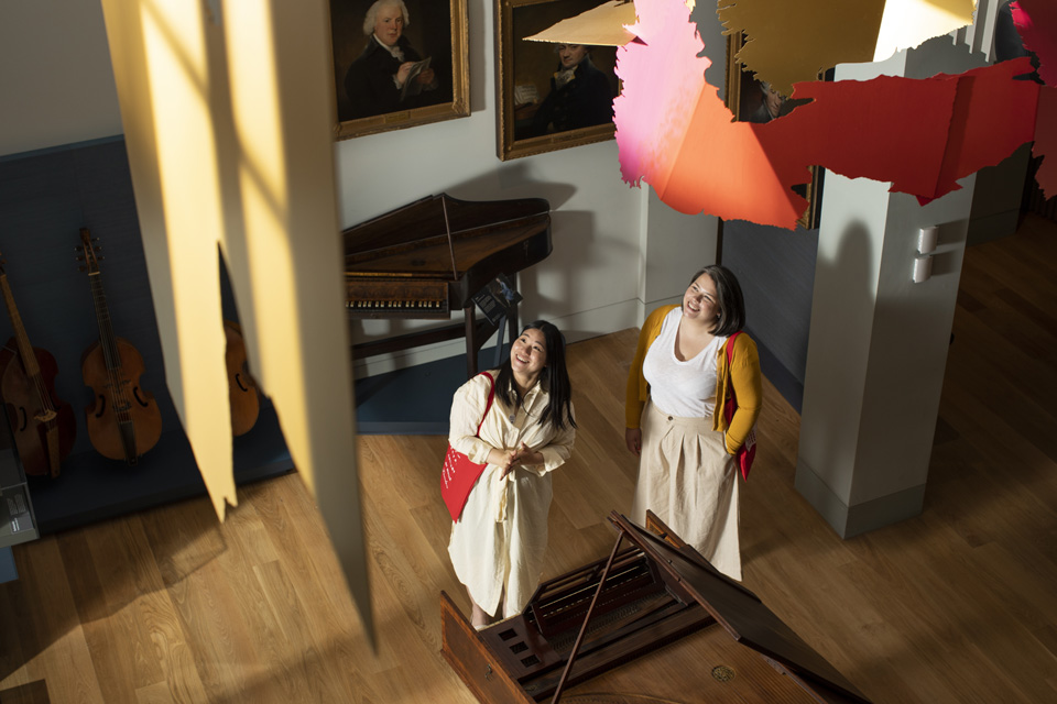 Two people in the RCM Museum next to instruments, looking up at the artwork