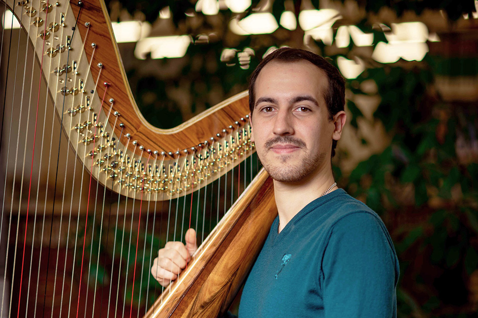 Viktor Hartobanu rests his harp on his shoulder and smiles