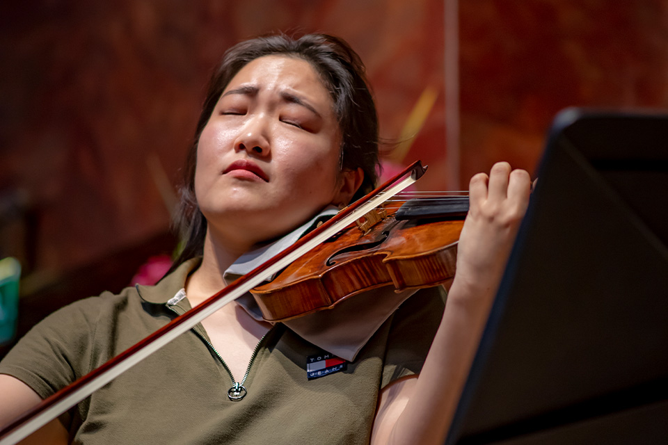 A woman plays the violin expressively, her eyes closed