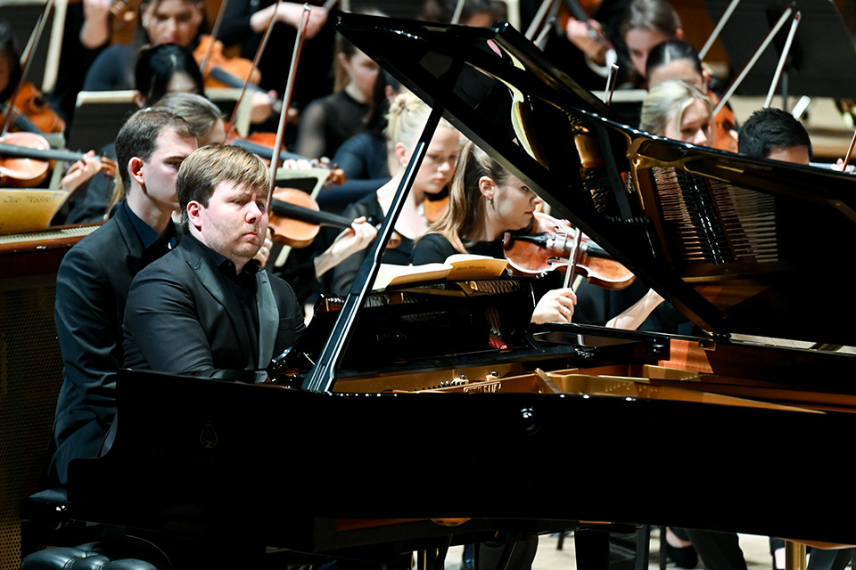 Thomas Kelly plays the piano on stage, an orchestra behind him