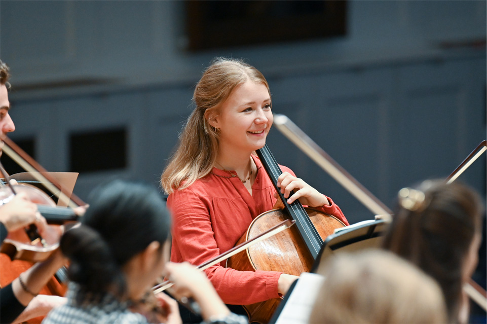 Female student enjoying herself and playing the cello in an orchestra. Female student enjoying herself and playing the cello in an orchestra.