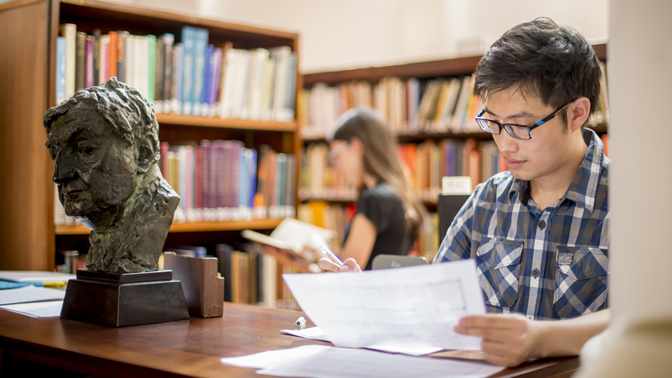 A male student, with glasses, editing a score in the library