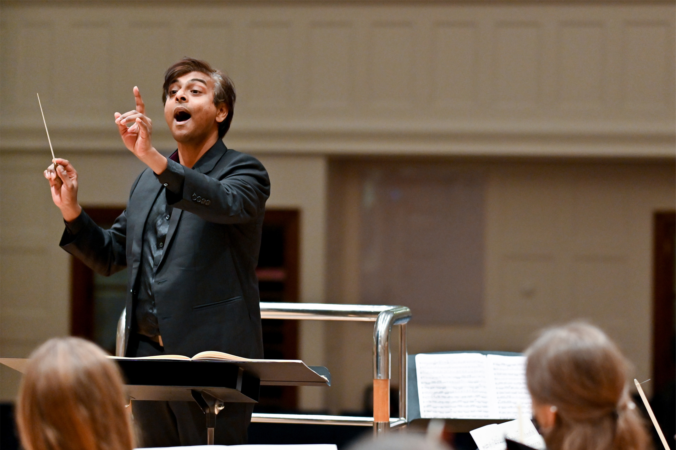 Male student, conducting a rehearsal for an upcoming orchestra, with musicians in the foreground in RCM's Amaryllis Fleming Concert Hall