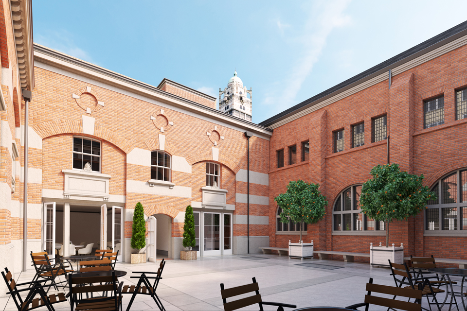 A red and white brick enclosed courtyard, with small trees to the right and wooden chairs and tables to the left.