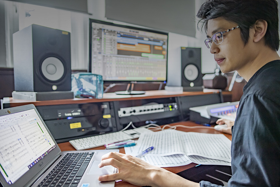 A male student looking at a computer screen, with papers on the background, trying to compose something.