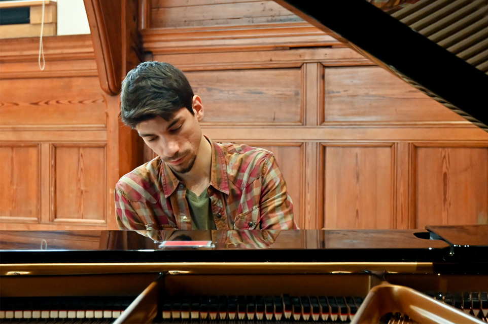 Male student playing the piano in the Parry rooms, a wooden panelled room.