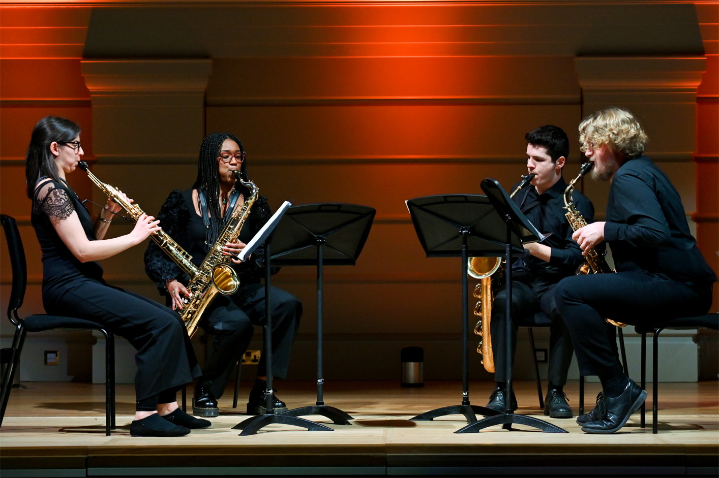 Group of students performing saxophones on stage, wearing smart black clothing.