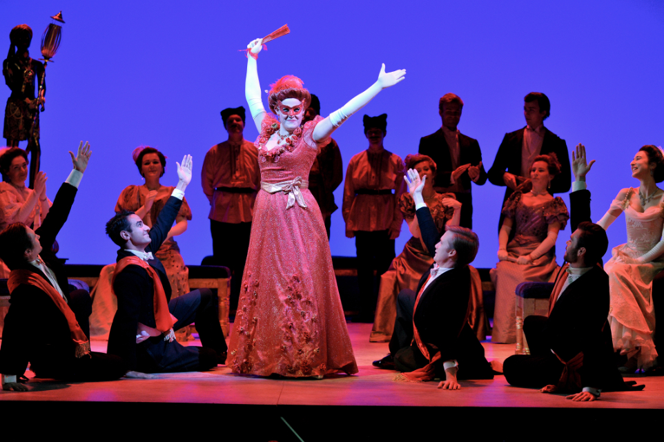 A female opera singer, striking a pose in a Victorian red dress, surrounded by male singers, kneeling down, striking a pose.