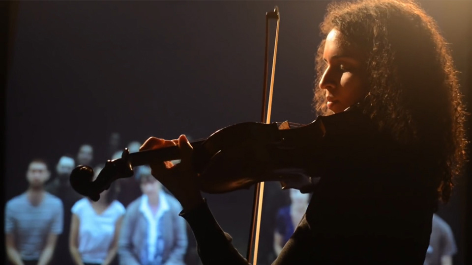 A women playing the violin in silhouette, with the audience in the background. A women playing the violin in silhouette, with the audience in the background.