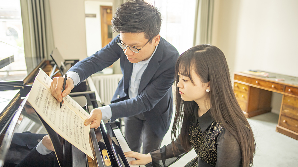 An Asian man teaching a female Asian student, practising on the piano. An Asian man teaching a female Asian student, practising on the piano.