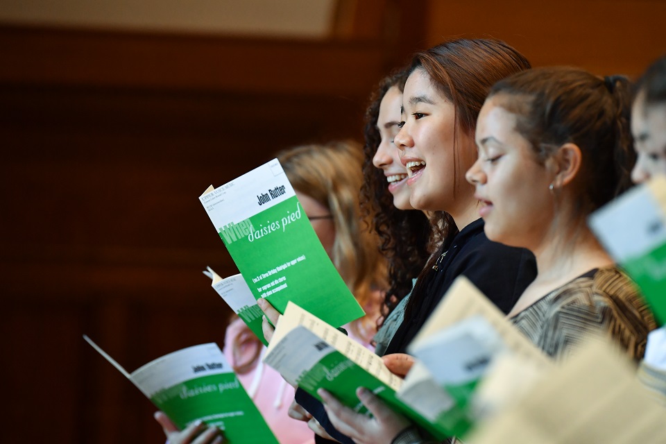 A group of young RCMJD students, singing, holding green music books.
