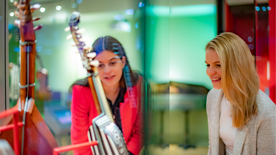 Two adult white female students looking at an exhibit, in a brightly lit room at the Royal College of Music museum. Two adult white female students looking at an exhibit, in a brightly lit room at the Royal College of Music museum.