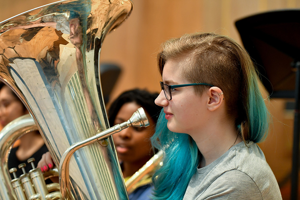 A female RCMJD student with tuba, sitting in rehearsal.
