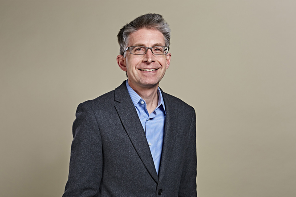 A white man, with glasses, smiling at the camera and wearing a suit.
