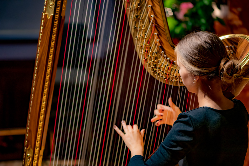 A female student, wearing a black top, playing the harp.