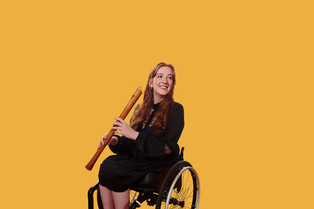 A female student, wearing smart black attire, holding a historical recorder, smiling at the camera, sitting in a wheelchair.