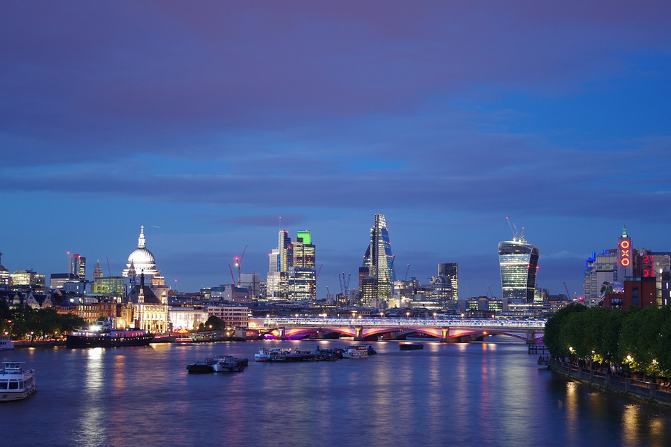 The evening London skyline, with buildings lit up, overlooking the Thames.