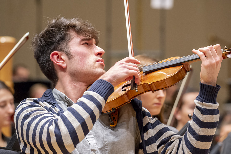 A male student performing on the violin in a rehearsal.
