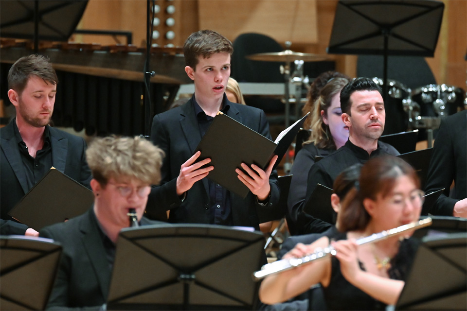 Male student singing with the rest of a chamber choir, rehearsing for a performance.